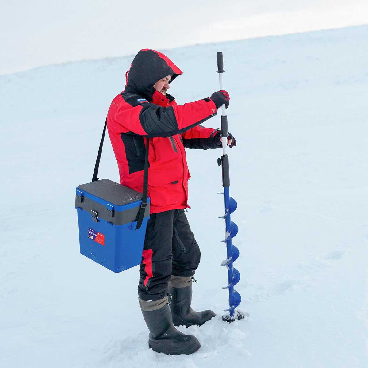 An angler carrying the Ice Fishing Bucket Type Box with Seat and Adjustable Shoulder Strap | 2 compartments | 5 gal | blue color and Classic hand auger