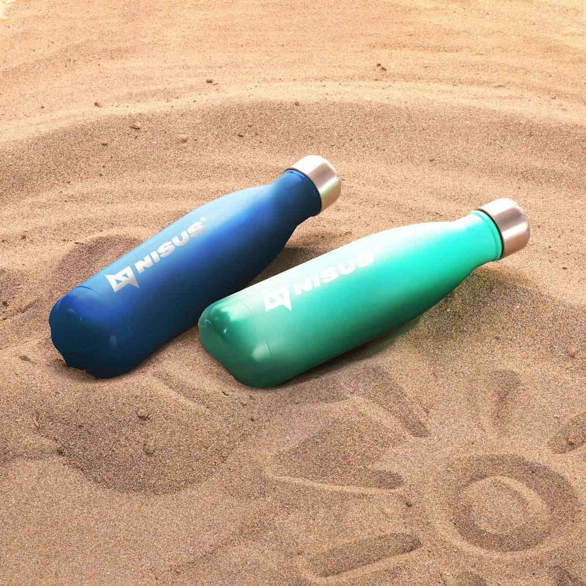 A couple of 17 oz stainless steel water bottles, blue and turquoise, lying on the sand