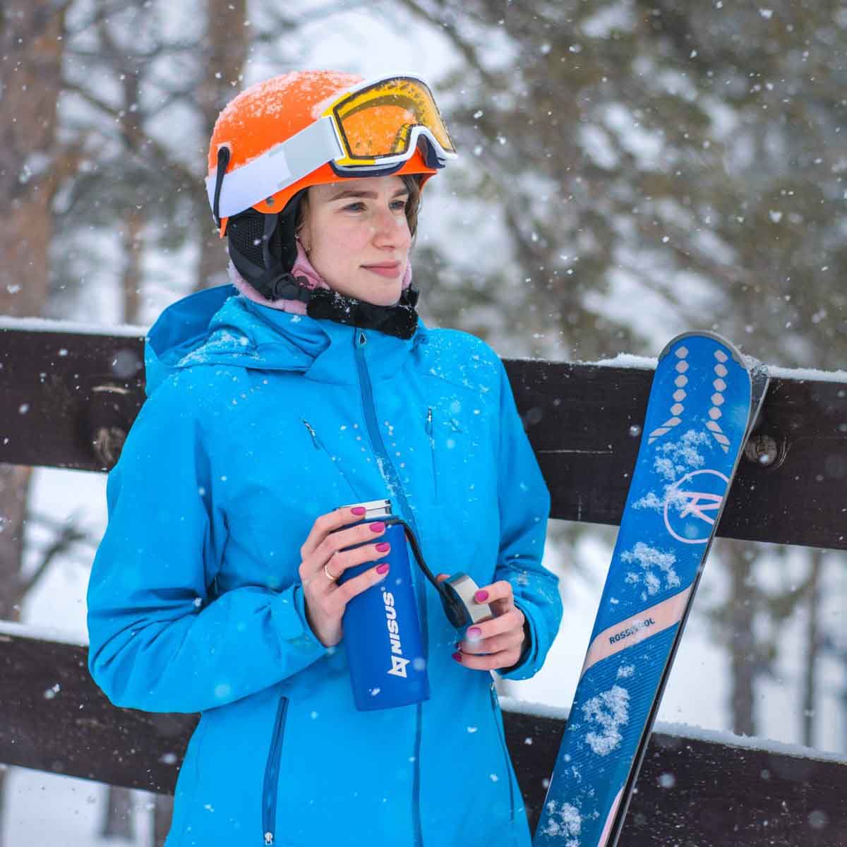 A girl wearing a ski suit and a helmet holding a Stainless Steel Insulated Sport Water Bottle with 3 Lid Types, 18 oz, blue