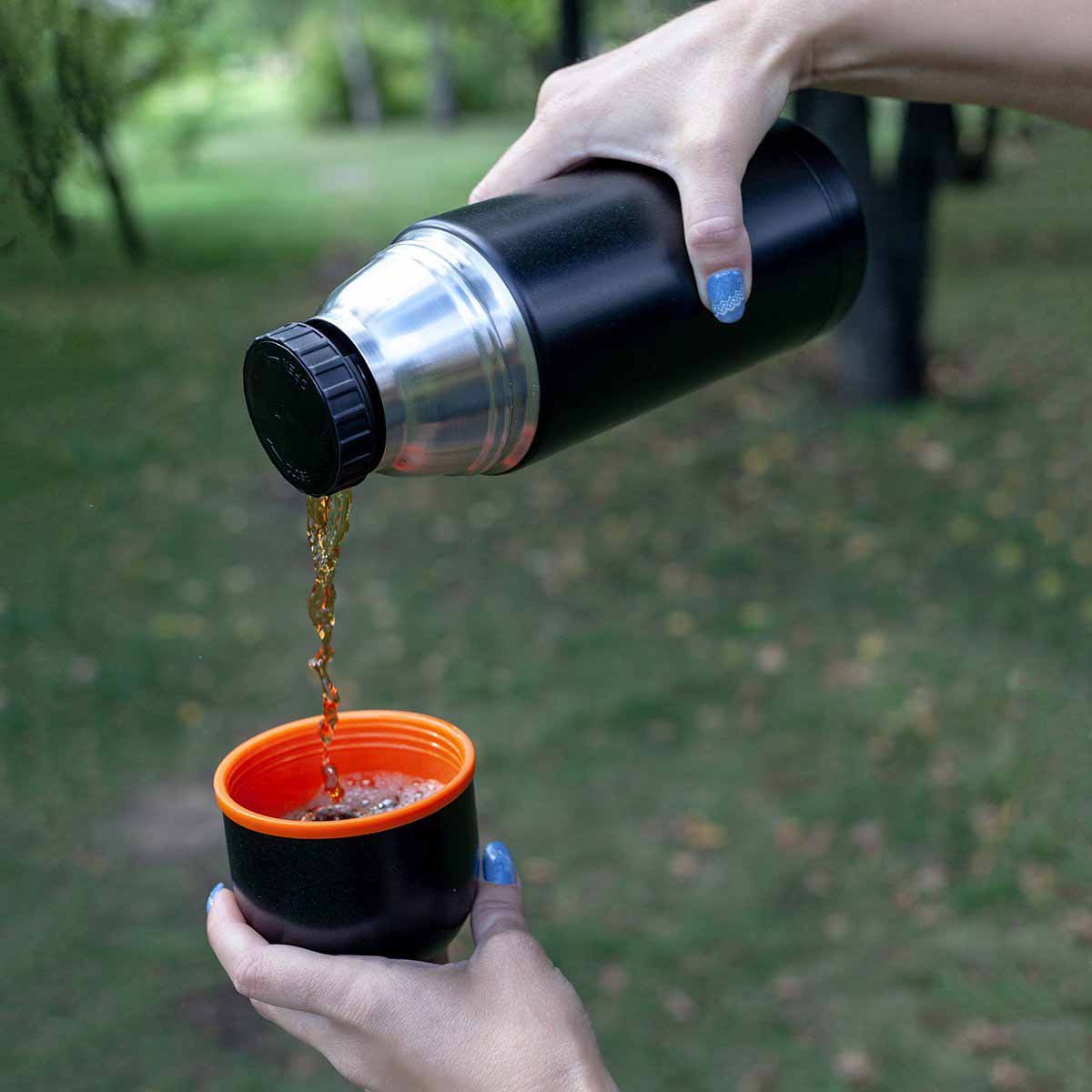 A girl pouring drinks from Big Stainless Steel Vacuum Flask with 2 Lid Cups, 40 oz, Black into a lid cup